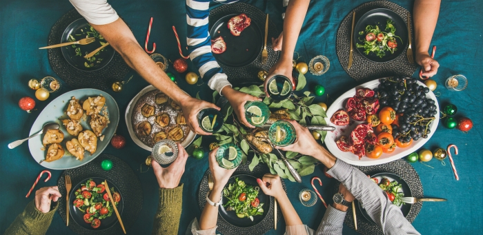 Company of friends of different ages or family gathering for Christmas or New Year party dinner at festive table. Flat-lay of human hands holding glasses with drinks, feasting and celebrating holiday together, top view.