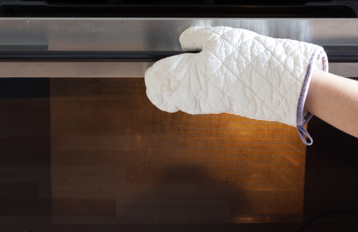 Woman hand in potholder opening the oven door